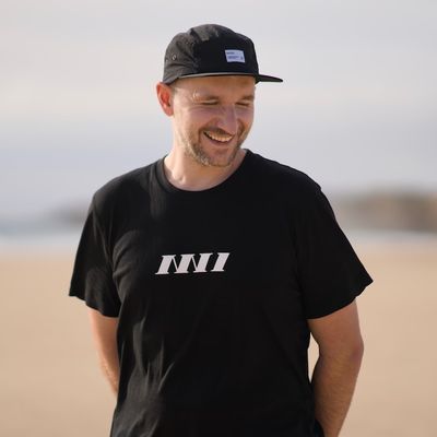 Portrait of smiling Paweł Grzybek, wearing an NN1 Dev Club t-shirt, standing on the beach.